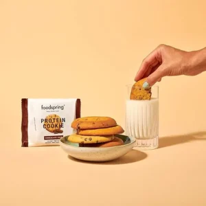Galletas proteicas foodspring con chips de chocolate acompañadas de un vaso de leche