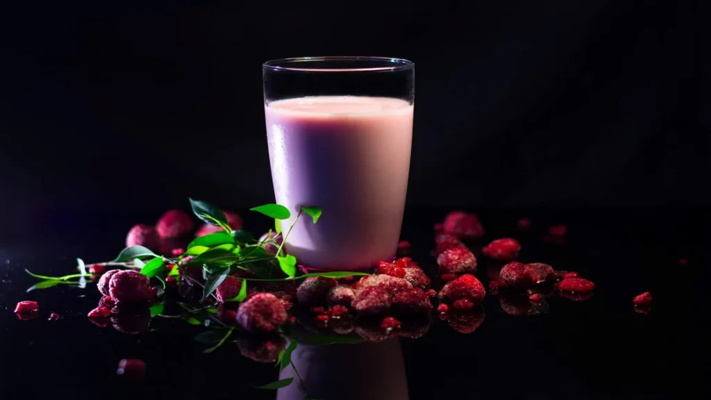 Batido sustitutivo Foodspring de frutos rojos con fondo oscuro y frutas congeladas.