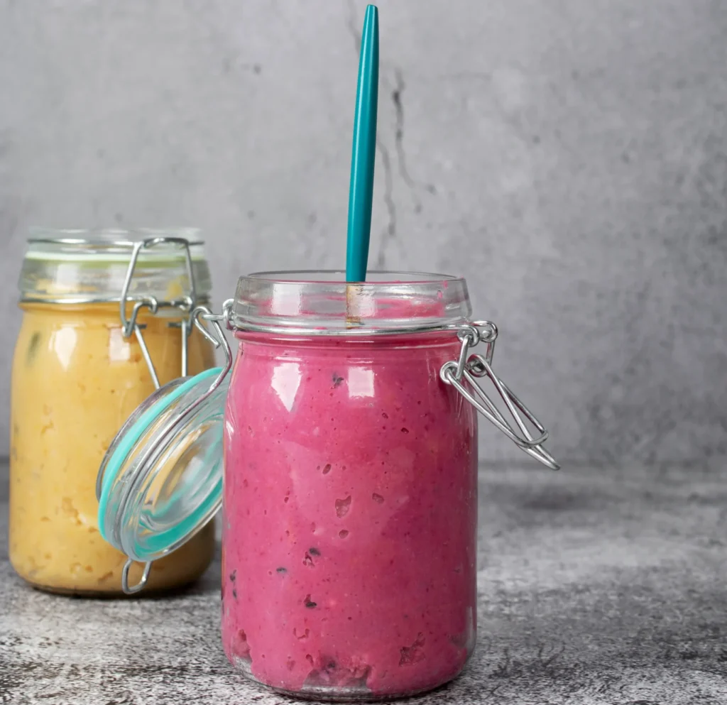 Dos batidos sustitutivos servidos en tarros de cristal, uno de color rosa y otro amarillo, sobre fondo gris.