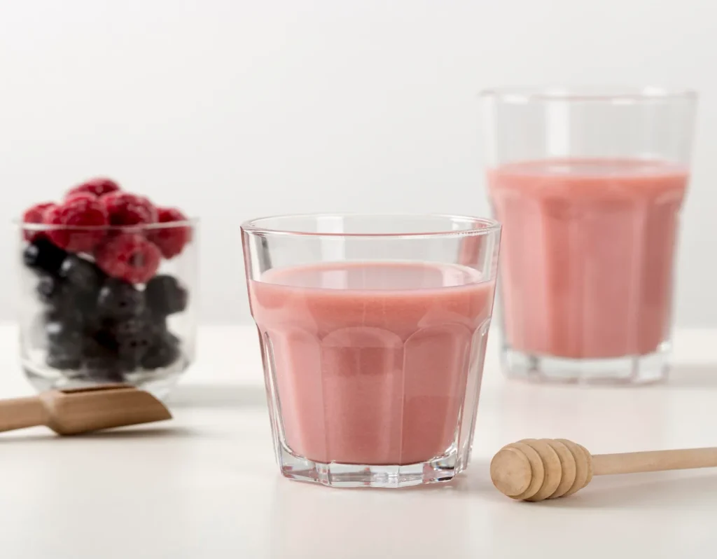 Vaso de batido sustitutivo vegano de frutos rojos junto a frambuesas y moras frescas.